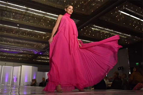 Fashion model struts the stage in a bright pink, flowy gown designed by local Long Beach designer Roger Canamar.