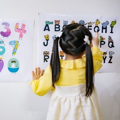 Child points at outline of letters on a classroom wall.