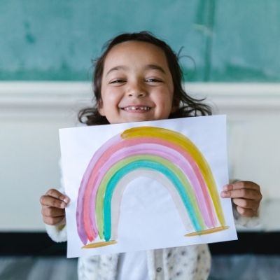 little girl holding up and showing rainbow painting