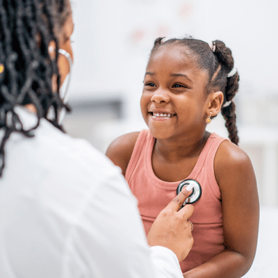 Young girl smiling while getting her heart checked by her primary care doctor.