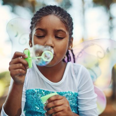 Young girl in fairy costume blowing bubbles in nature.