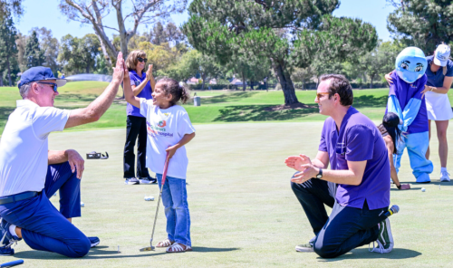 Kataleya Suazo, a 6-year-old in remission from Ewing sarcoma, celebrates sinking her ball as she putts alongside Millie the Dolphin, Miller Children’s & Women’s Hospital’s mascot (back, right) during the 16th Annual Champion’s Club Classic Golf Tournament at Virginia Country Club. 