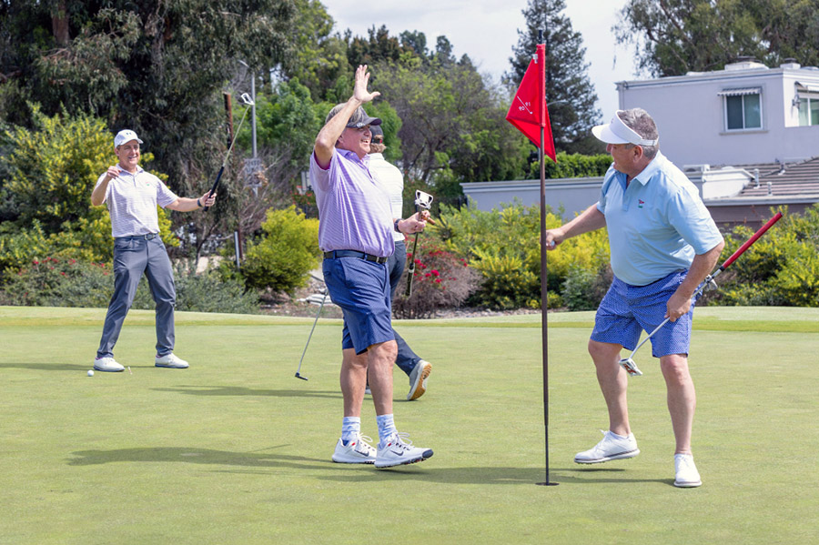 Three golf participants smile and high-five during the tournament.