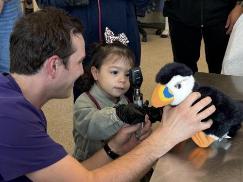 John Logie, child life specialist at Miller Children’s & Women’s Hospital, helps 2-year-old Gabriella Alfaro carefully check the eyes of a stuffed puffin plush during a hands-on educational experience at the Aquarium of the Pacific’s Molina Animal Care Center.