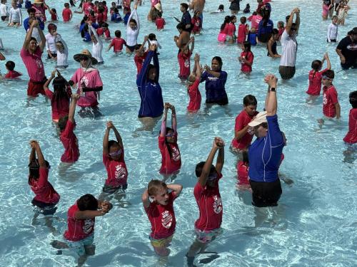 With arms outstretched toward the sky, young swimmers at Wild Rivers practice basic stroke techniques during a hands-on water safety session at the World’s Largest Swimming Lesson, sponsored by MemorialCare.
