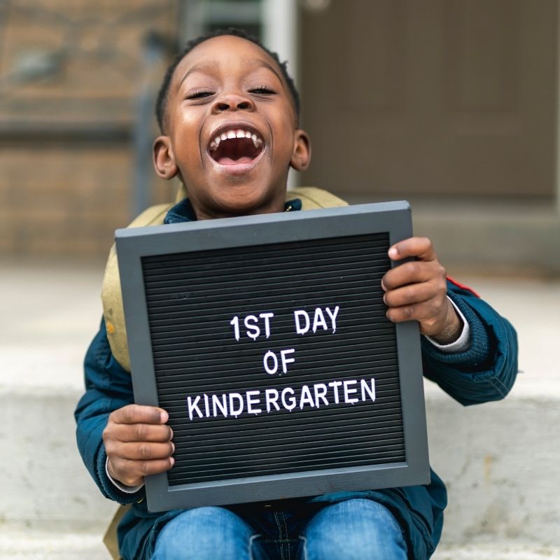 smiling black boy holding up a sign that says "1st day of kindergarden"