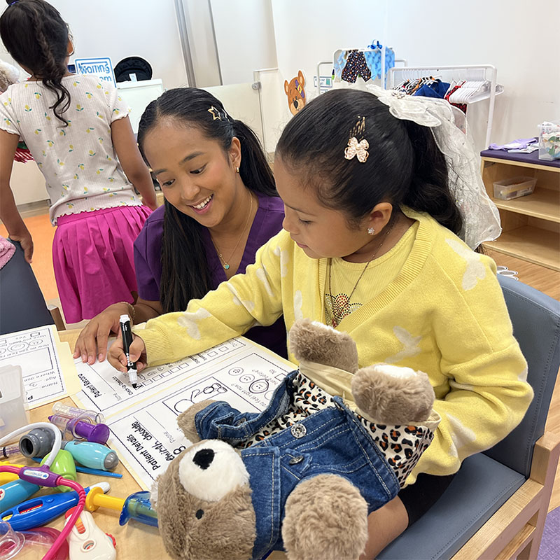a little girl doing an activity worksheet in a playroom sounded by toys