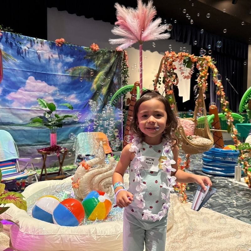 Serena enjoys summer fun beside an inflatable pool filled with beach balls and bubbles during Beach Day at Miller Children’s & Women’s Hospital.