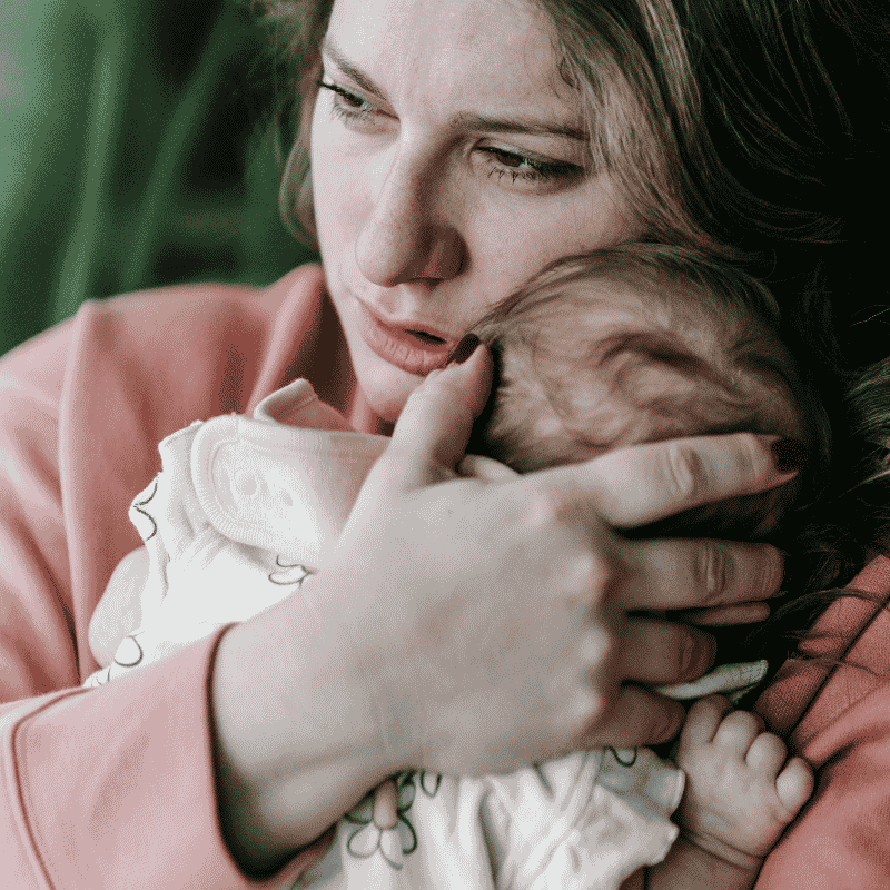 Mom holding infant looking worried. 